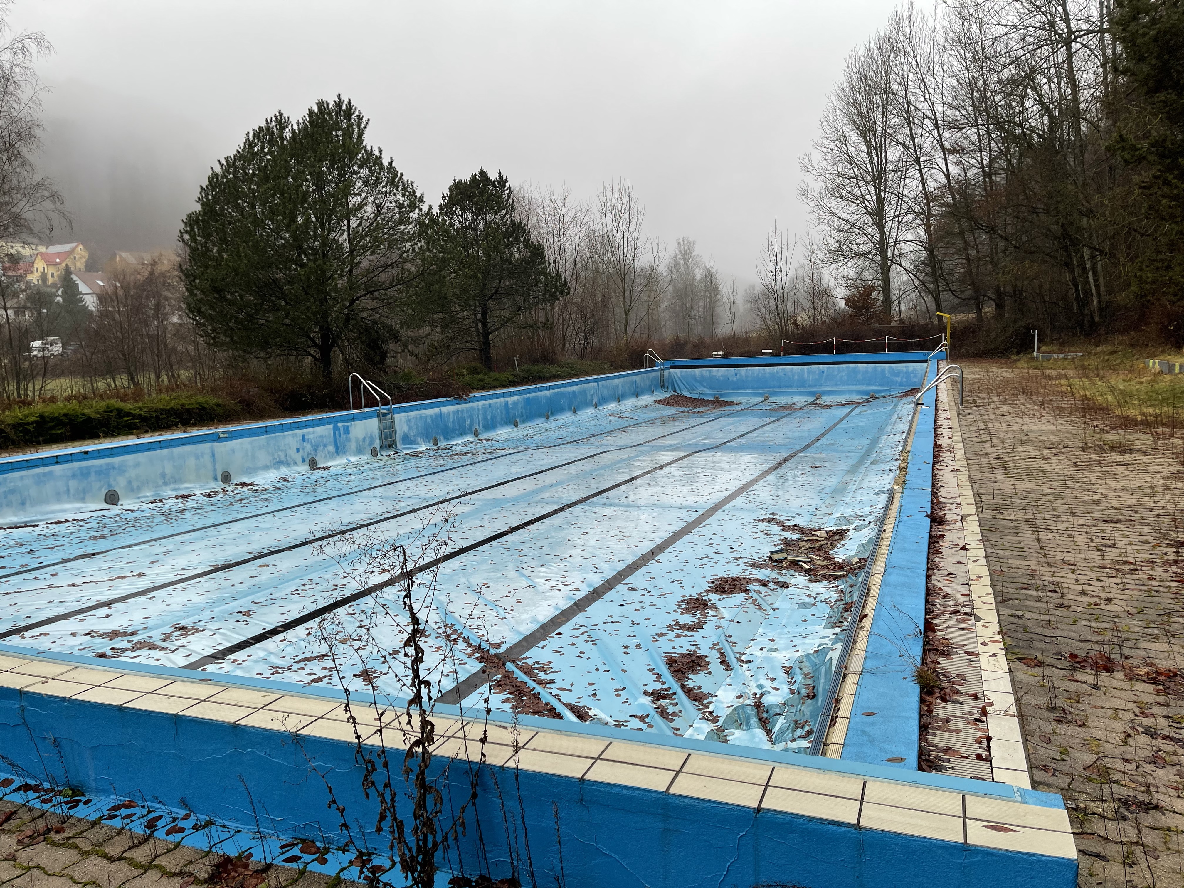 Das Bild zeigt ein leeres, verschmutztes Schwimmbecken im Winter.