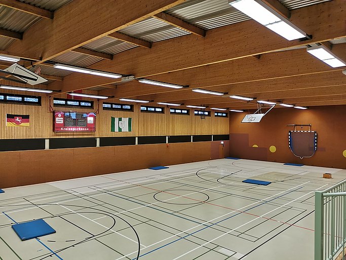 Man sieht eine Sporthalle von Innen. Der Boden ist mit Markierungen überzogen, darauf liegen blaue Matten.