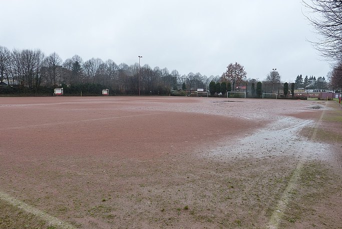 Das Bild zeigt einen Sportplatz vor der Sanierung. Im Hintergrund sind Fußballtore zu sehen.