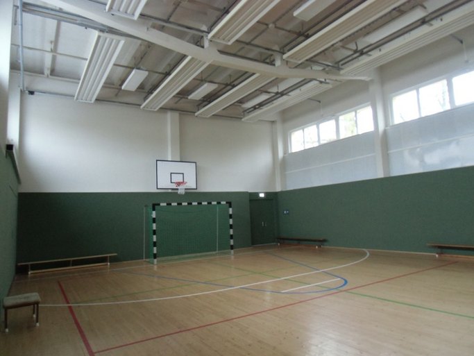 Das Bild zeigt eine Turnhalle mit Dielenboden, Tor und Basketballkorb.