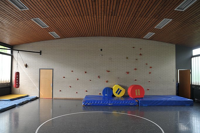 Das Bild zeigt eine Turnhalle mit Kletterwand und Sportmatte von innen.