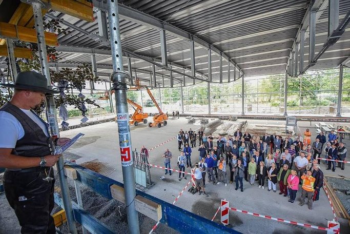 Das Bild zeigt einen Mann in Handwerksgewand auf einem Baugerüst, der zu einer versammelten Menge an Menschen spricht.