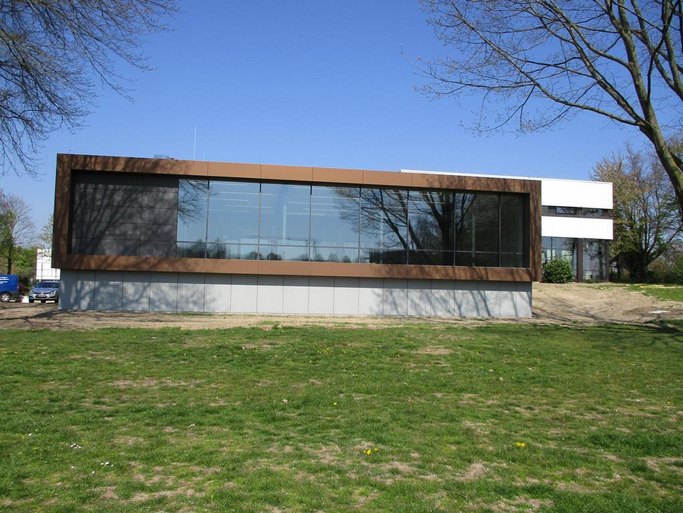 Das Bild zeigt ein Gebäude mit Flachdach und Fensterfront in Richtung einer Wiese.