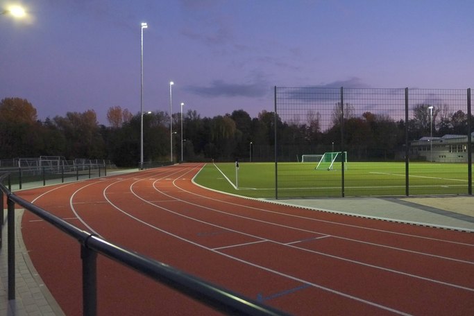 Das Bild zeigt eine Sportanlage mit Fußballfeld und Laufbahnen mit Flutlichtanlage bei Dämmerung.