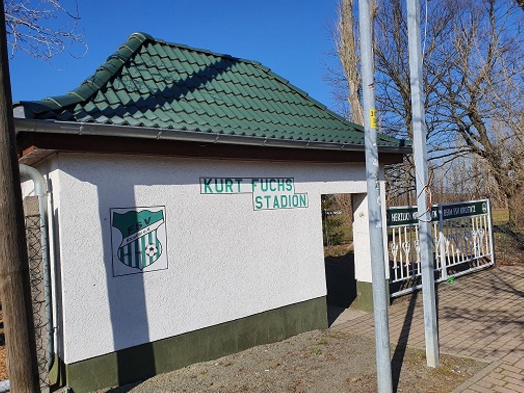 Das Bild zeigt einen Eingangsbereich mit einem weißen Gebäude, auf dem "Kurt-Fuchs-Stadion" steht.