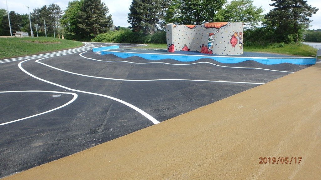 Das Bild zeigt einen Sportplatz mit Bodenwellen und Markierungen, im Hintergrund ist eine Boulderwand zu sehen.