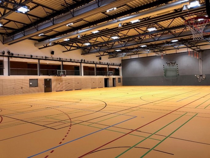 Das Bild zeigt eine beleuchtete Sporthalle mit gelbem Boden und bunten Markierungen.