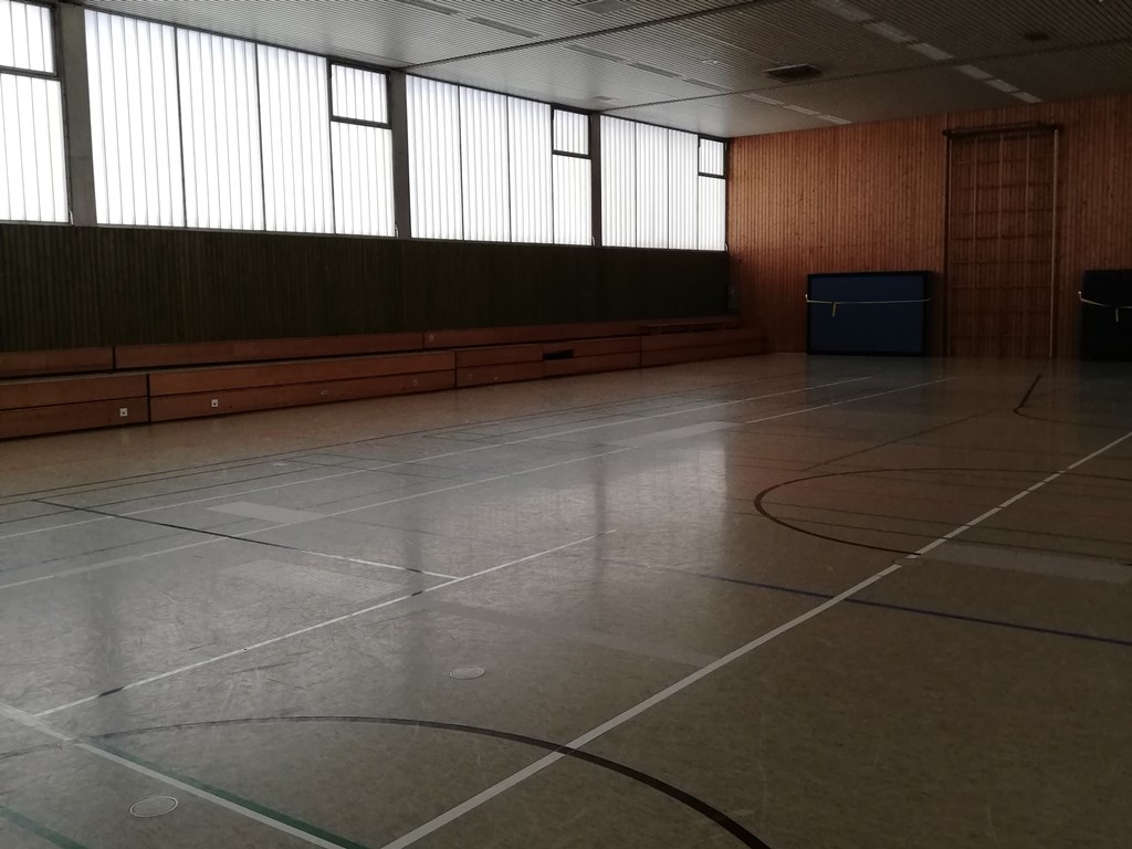 Man sieht eine Turnhalle von innen mit alten hohen Fenster durch die Licht eindringt.