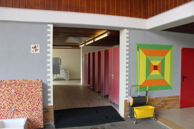 Das Bild zeigt den Eingang zu einem Umkleidebereich mit roten Kabinen.
