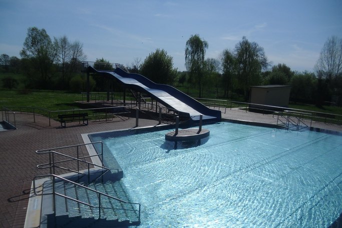 Das Bild zeigt ein Schwimmbecken in einem Freibad, in das eine Rutsche mündet.