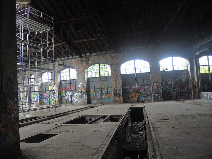 Das Bild zeigt eine leerstehende, baufällige Industriehalle mit Graffiti an den Wänden.