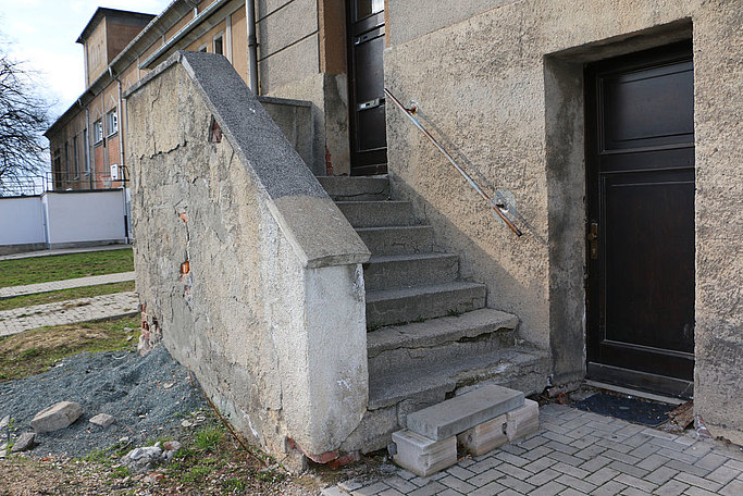 Das Bild zeigt einen Treppenaufgang an einem Gebäude in marodem Zustand.
