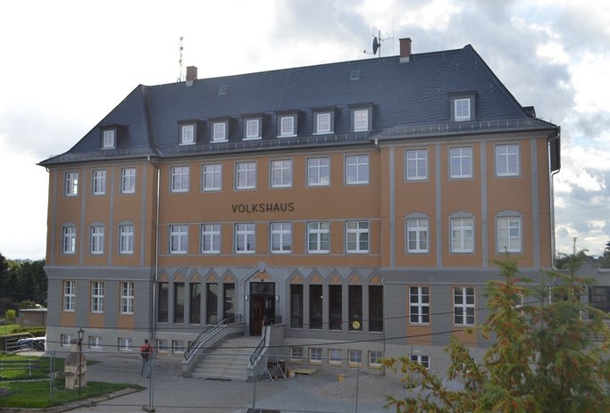 Das Bild zeigt ein freistehendes Gebäude mit orange-grauer Fassade und dem Schriftzug Volkshaus.