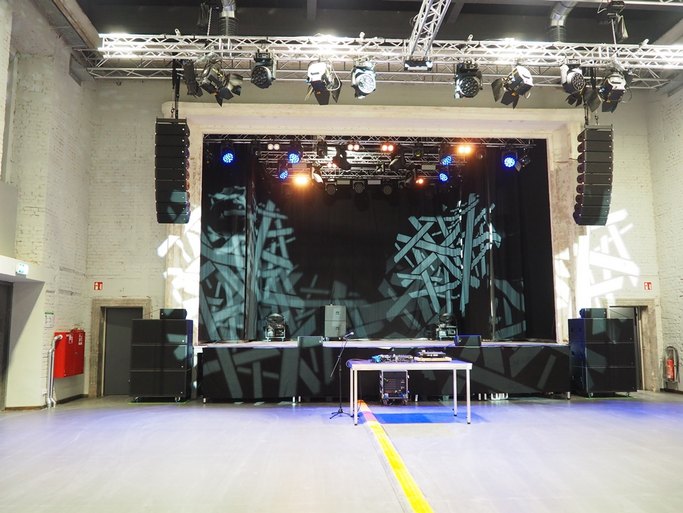 Das Bild zeigt eine mit Effekten beleuchtete Bühne, im Vordergrund ist ein tisch mit Technik-Equipment zu sehen.
