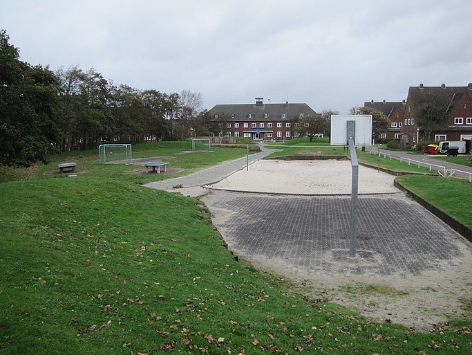 Das Bild zeigt verschiedene Sportanlagen auf einer Wiese, einen Sandbereich und einen Basketballkorb.