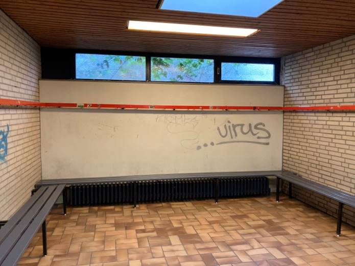 Man sieht eine Umkleidekabine mit einem Graffiti, welches "...virus" zeigt.