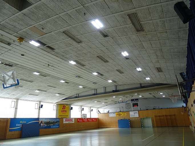 Das Bild zeigt eine Sporthalle mit holzverkleideten Wänden, verschiedenen Sportgeräten und Werbebannern.