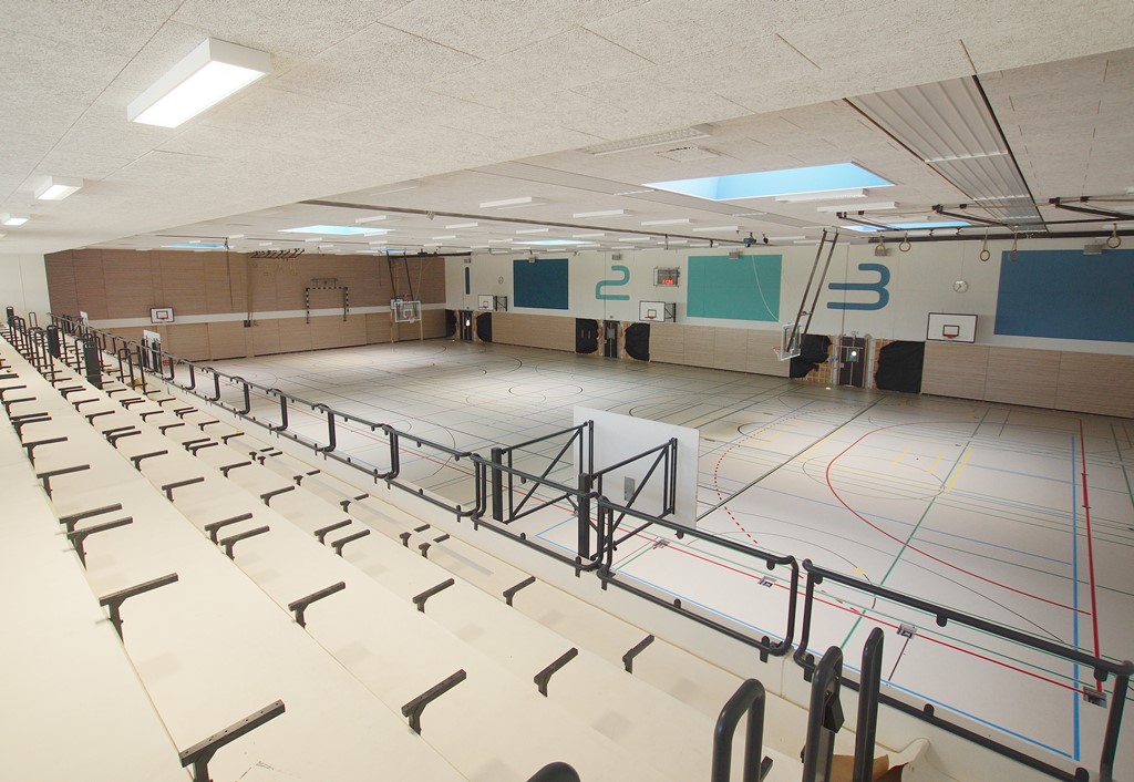 Das Bild zeigt die Innenansicht einer hellgestalteten Sporthalle mit Zuschauerrängen.