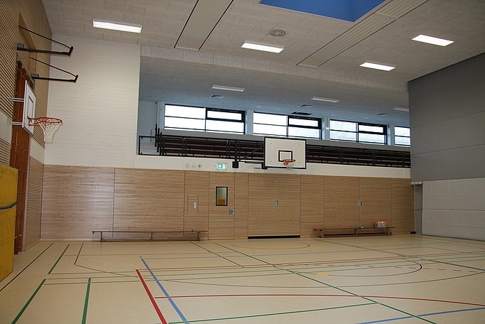 Das Bild zeigt einen abgetrennten Teil einer Sporthalle mit Basketballkörben und Langbänken.