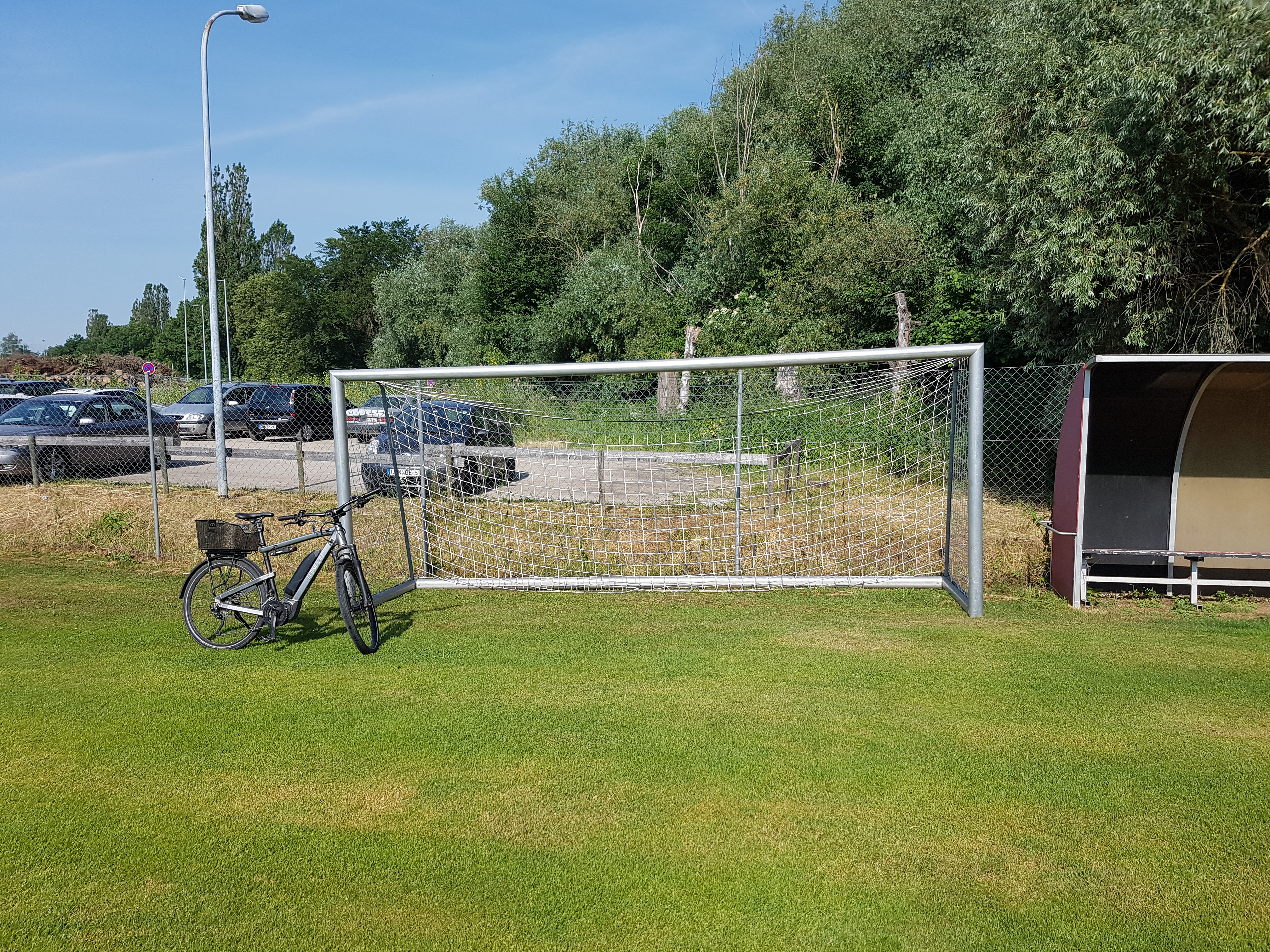 Das Bild zeigt einen Rasenplatz mit Tor und Trainerbank. Am Fußballtor lehnt ein Fahrrad.