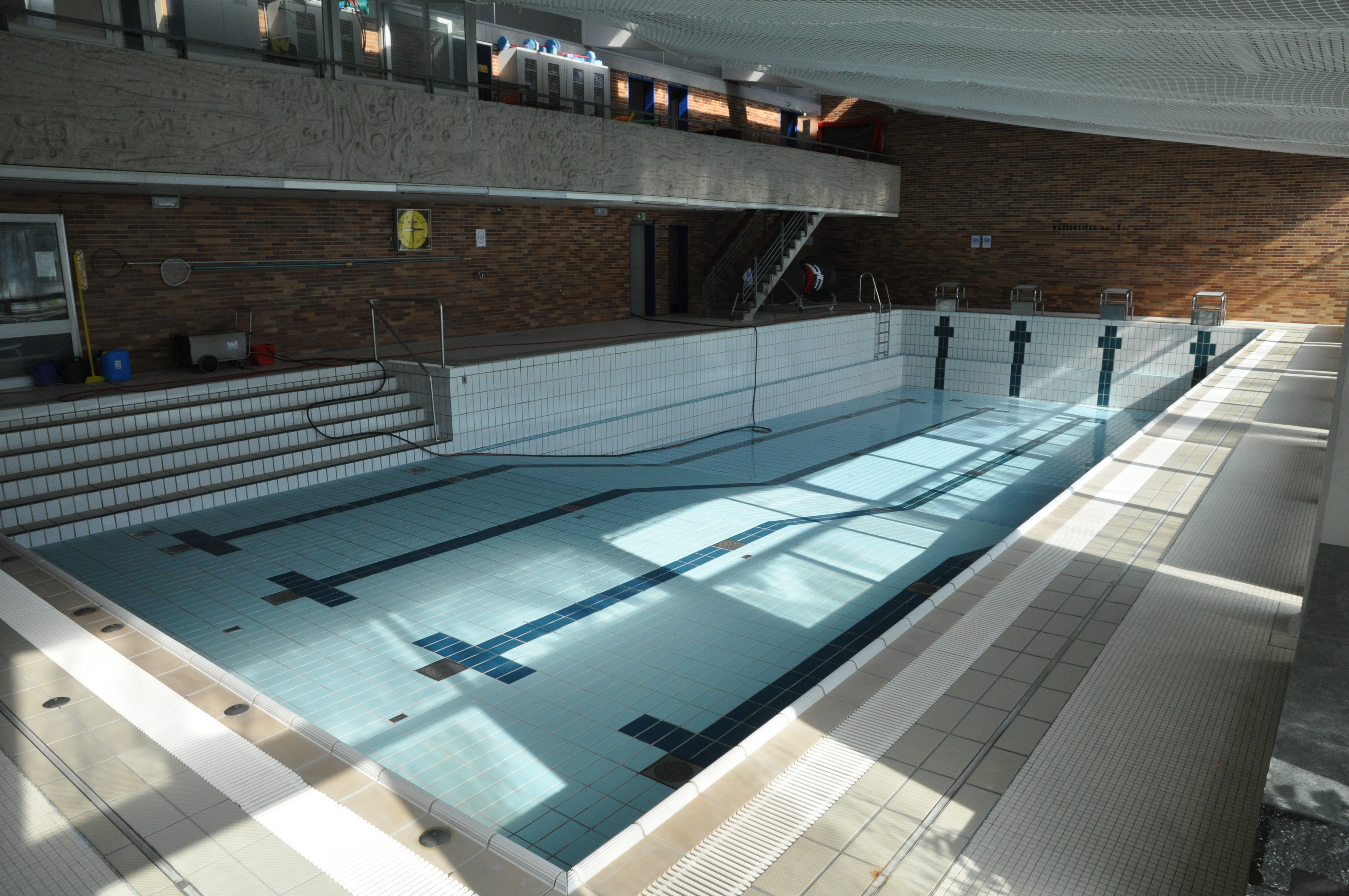 Das Bild zeigt ein leeres Schwimmbecken in einem Hallenbad.