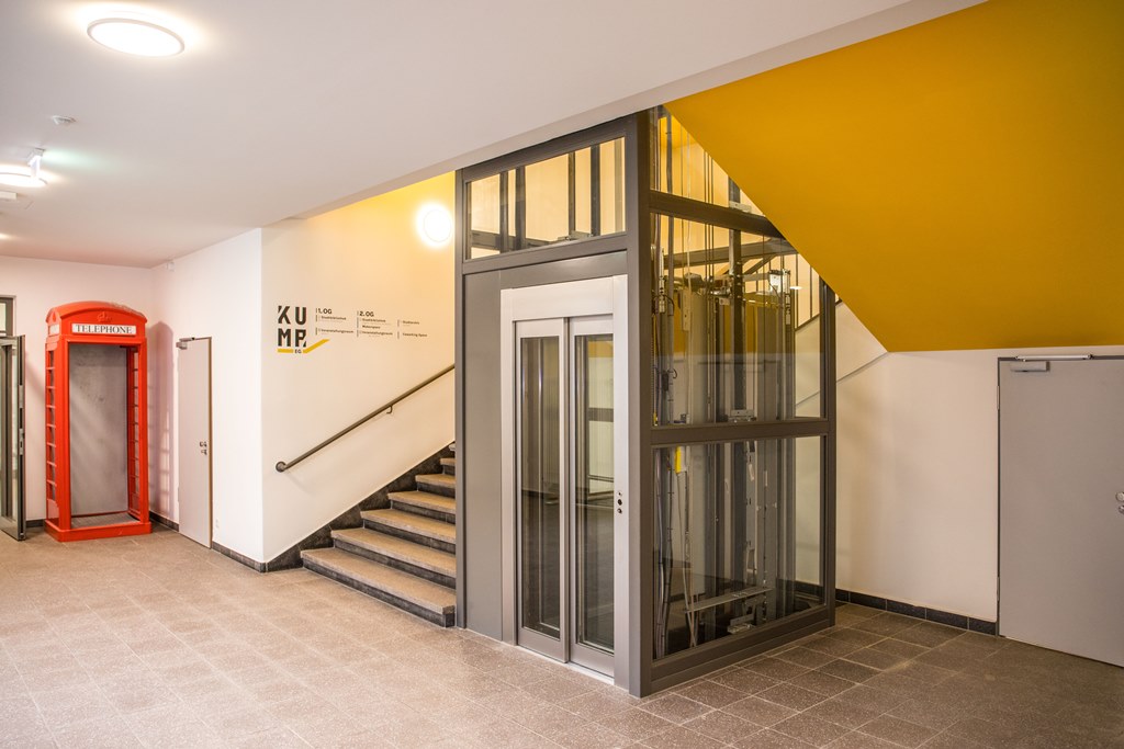 Das Bild zeigt einen Fahrstuhl sowie eine Treppe im Eingangsbereich.