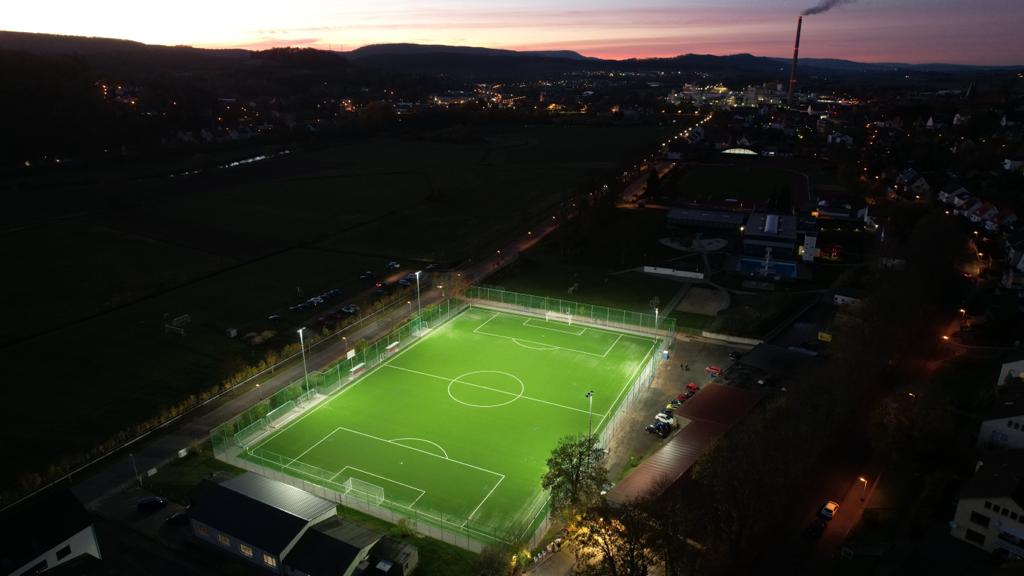Die Luftaufnahme zeigt ein beleuchtetes Fußballfeld bei Nacht.