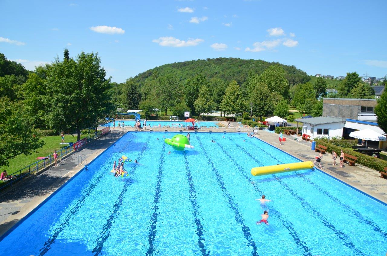 Auf dem Foto ist ein Schwimmbecken mit Menschen im Freien zu sehen. 