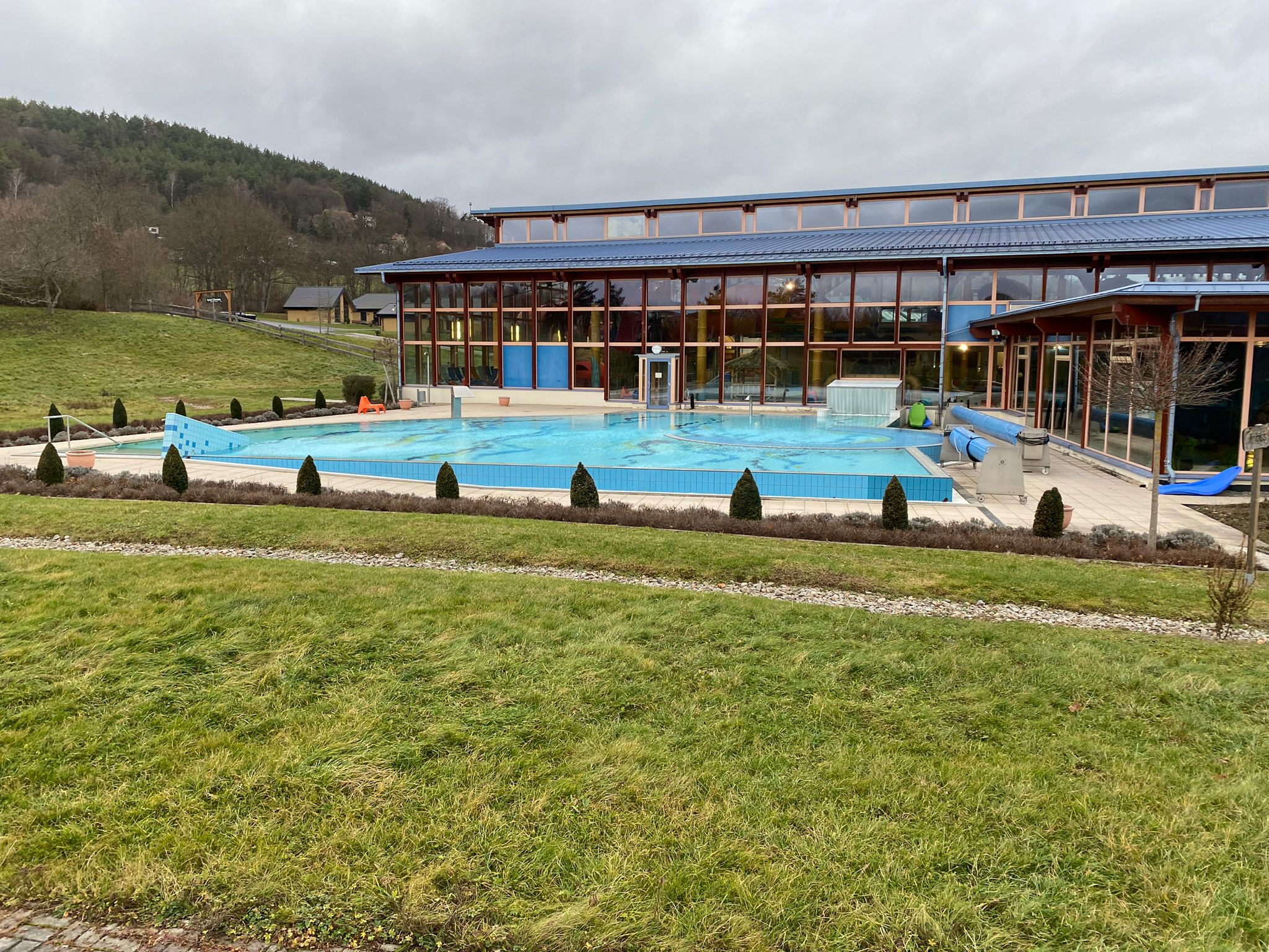 Das Bild zeigt das Außenbecken eines Schwimmbads. Im Hintergrund ist ein verglastes Gebäude zu sehen.