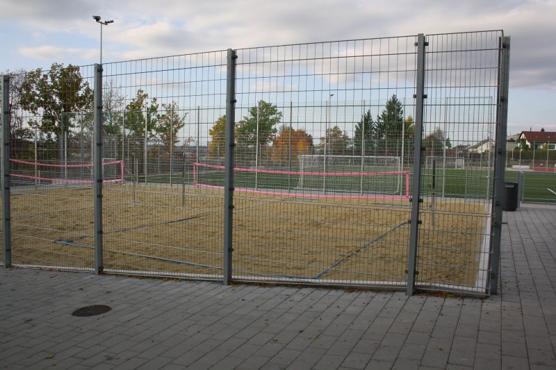 Das Bild zeigt zwei Beachvolleyballplätze mit Netzen. Der Platz ist von einem hohen Zaun umgeben.