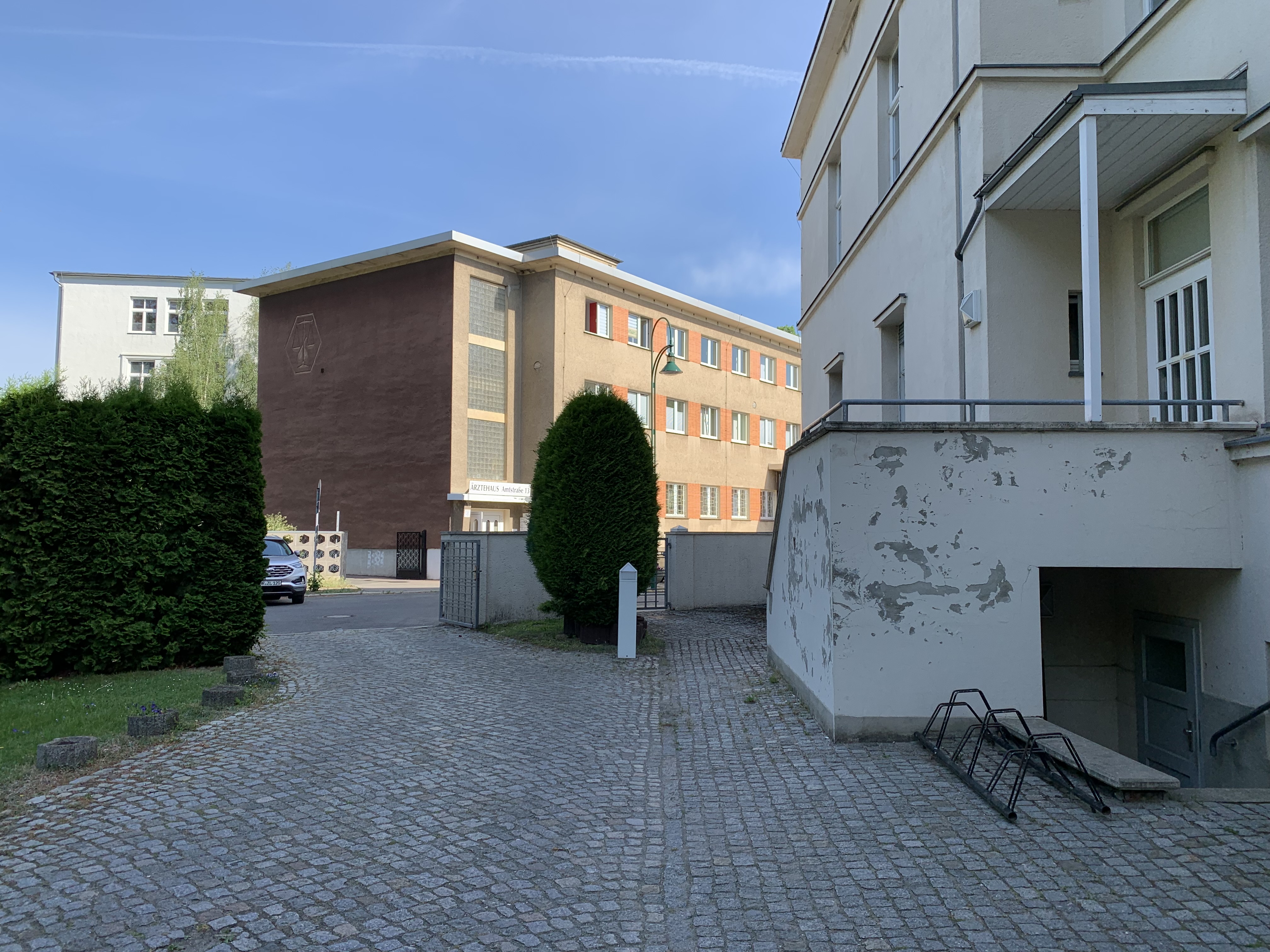 Das Bild zeigt zwei Gebäude von außen. Unten rechtes im Bild sind Fahrradständer zu sehen. Das Gebäude auf der rechten Seite ist sanierungsbedürftig.