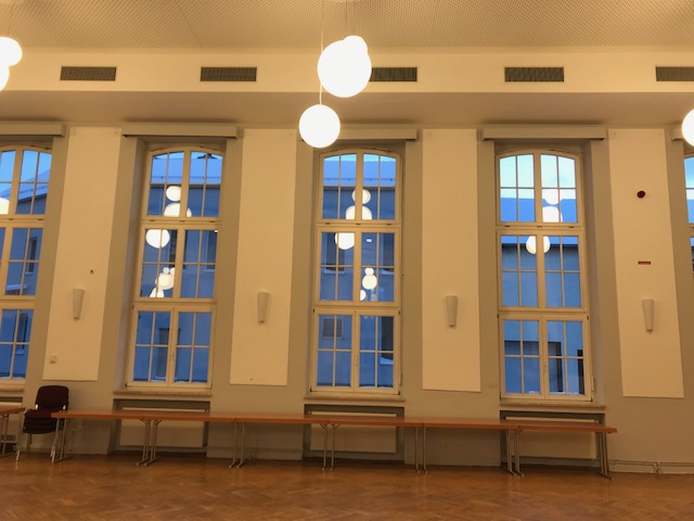 Auf dem Foto ist ein Saal mit hohen Fenstern zu sehen. 