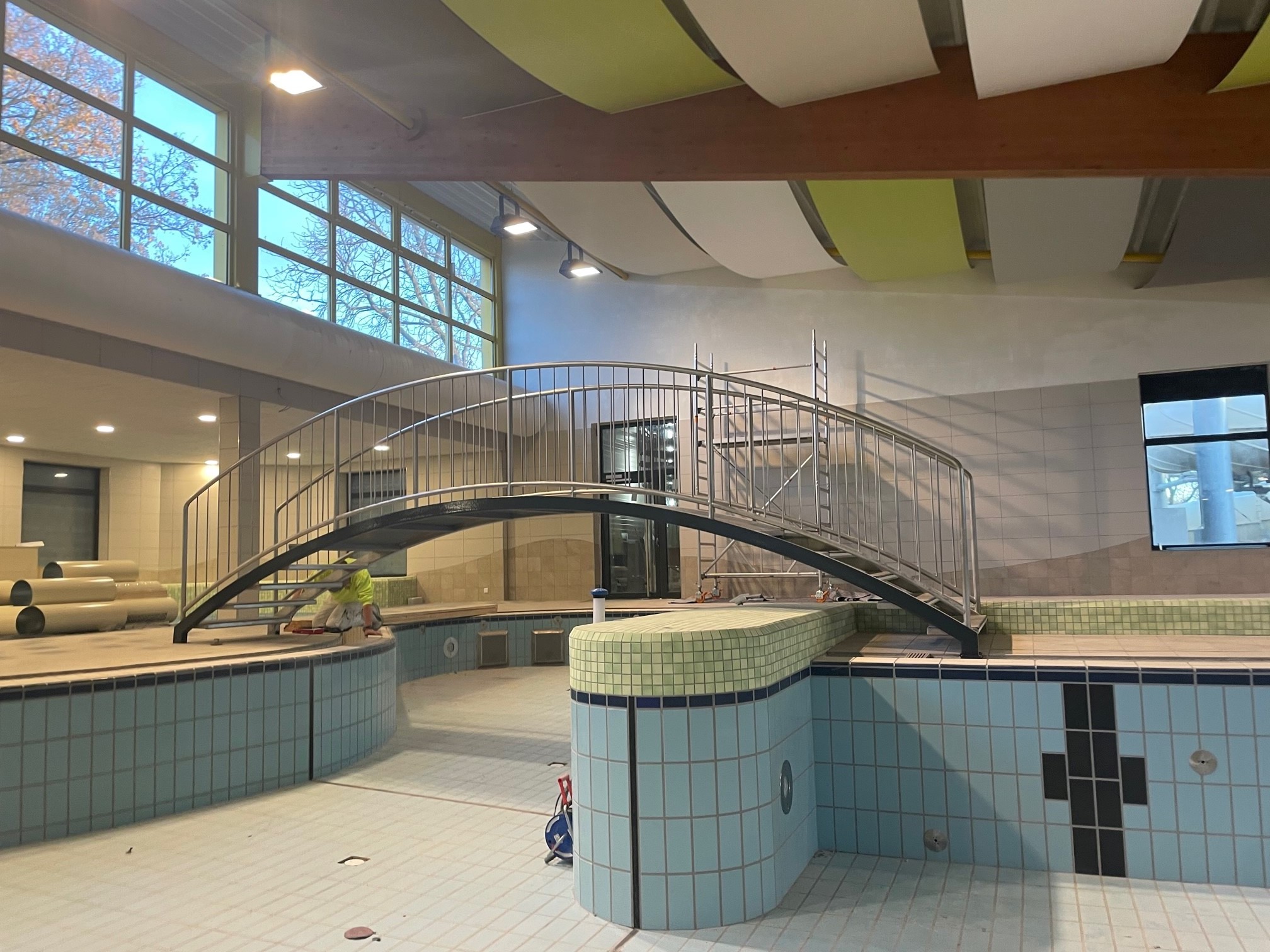 Das Bild zeigt ein leeres Schwimmbecken. Eine Brücke führt in den hinteren Teil des Hallenbades.