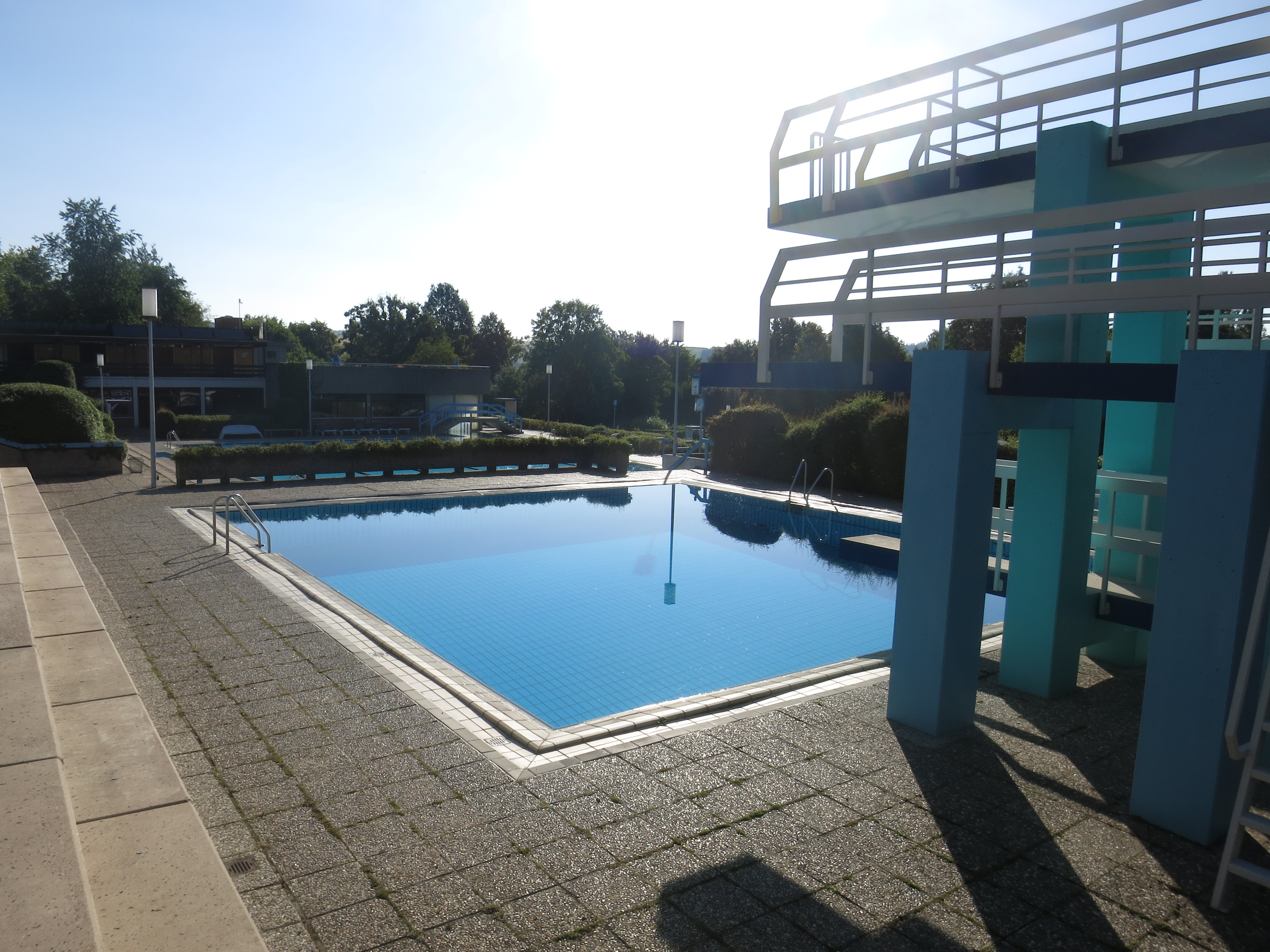 Das Bild zeigt ein Schwimmbecken in einem Freibad mit Sprungturm.