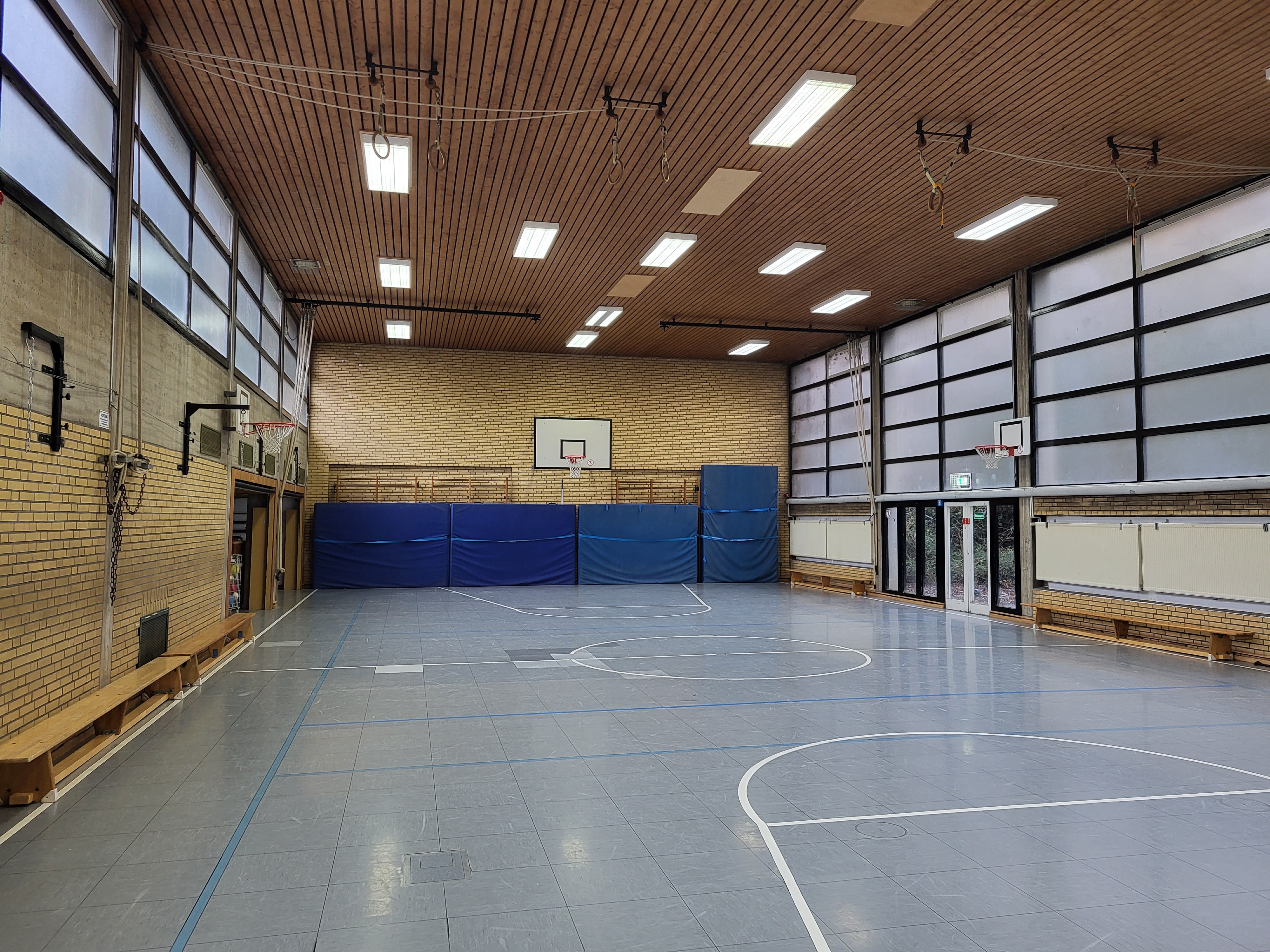 Das Bild zeigt eine Sporthalle von innen. An der Wand lehnen vier große blaue Matten.