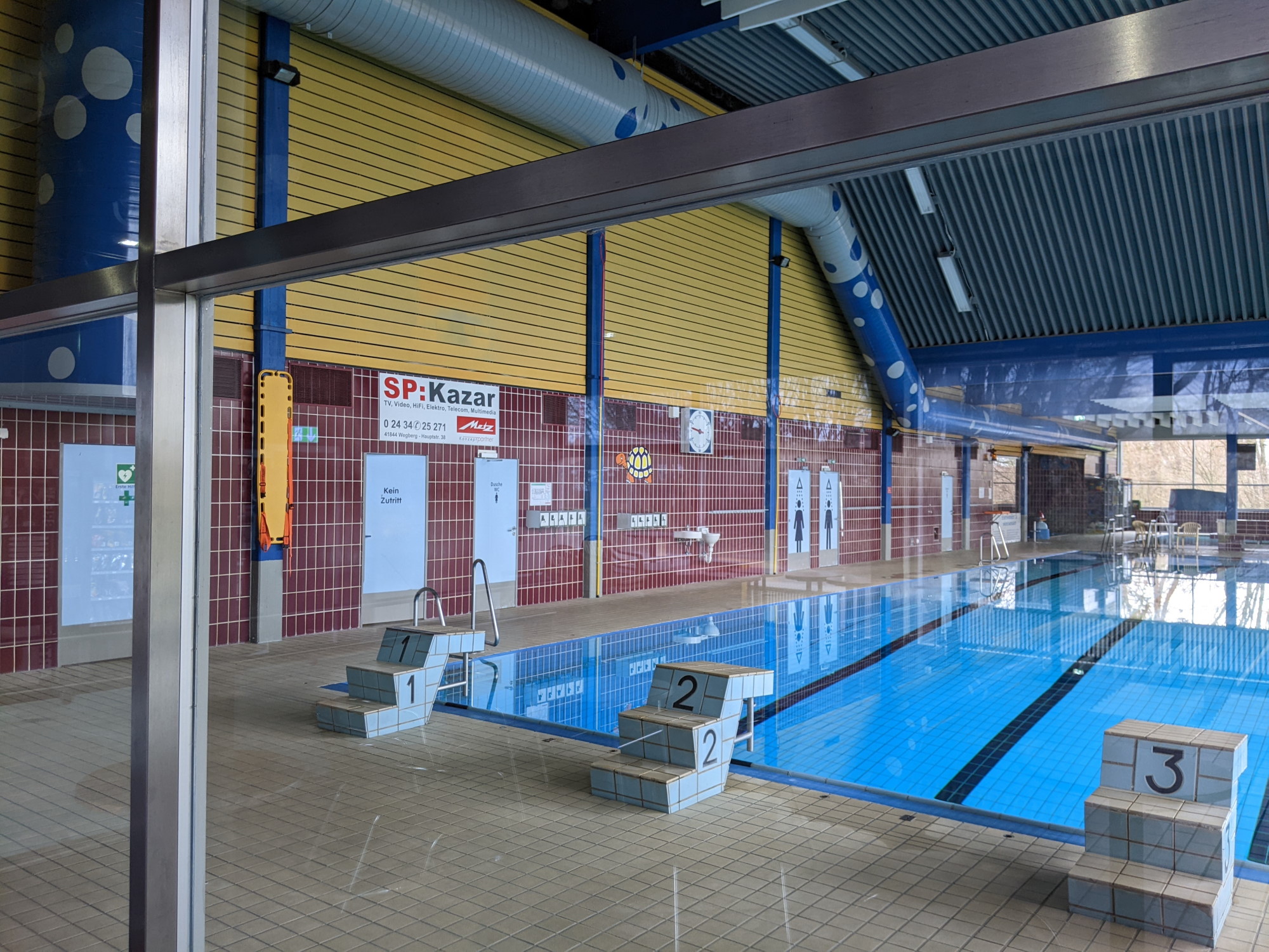 Das Foto zeigt eine Schwimmhalle mit drei Bahnen und Startblöcken.