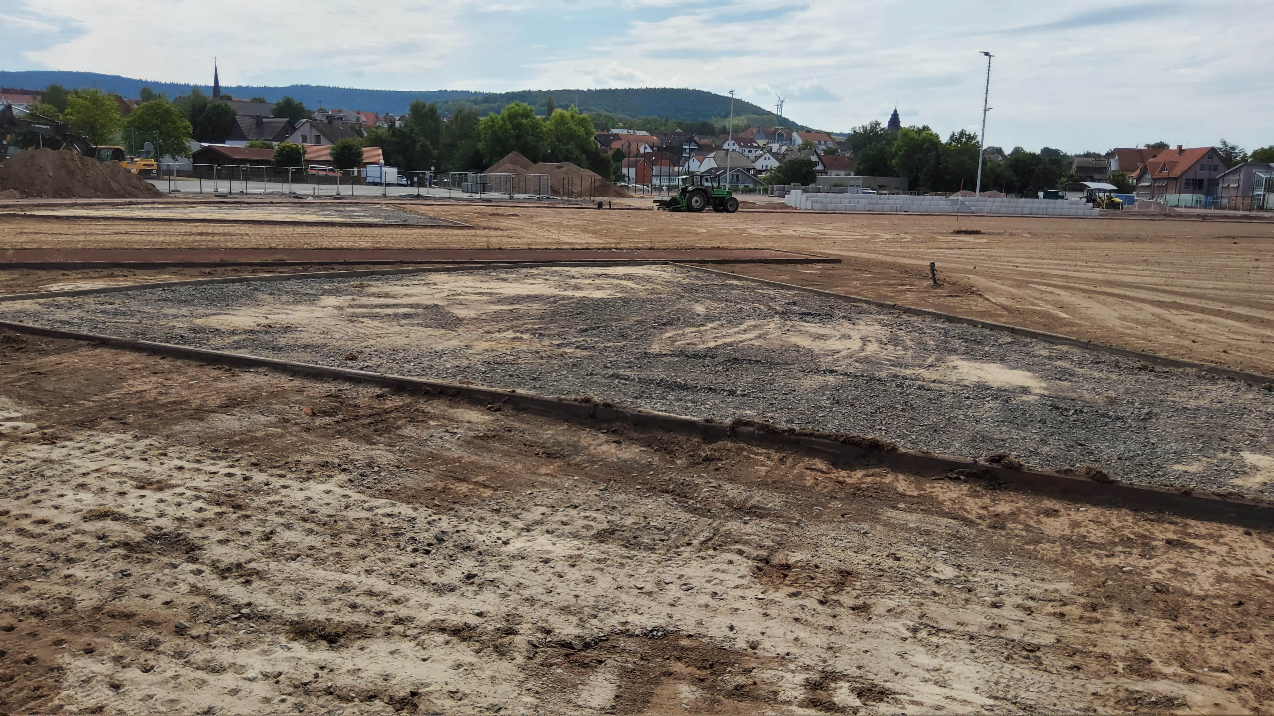 Das Bild zeigt eine Baustelle. Der Boden wurde abgegraben und ist mit Sand überzogen. Im Hintergrund sieht man eine Stadt.