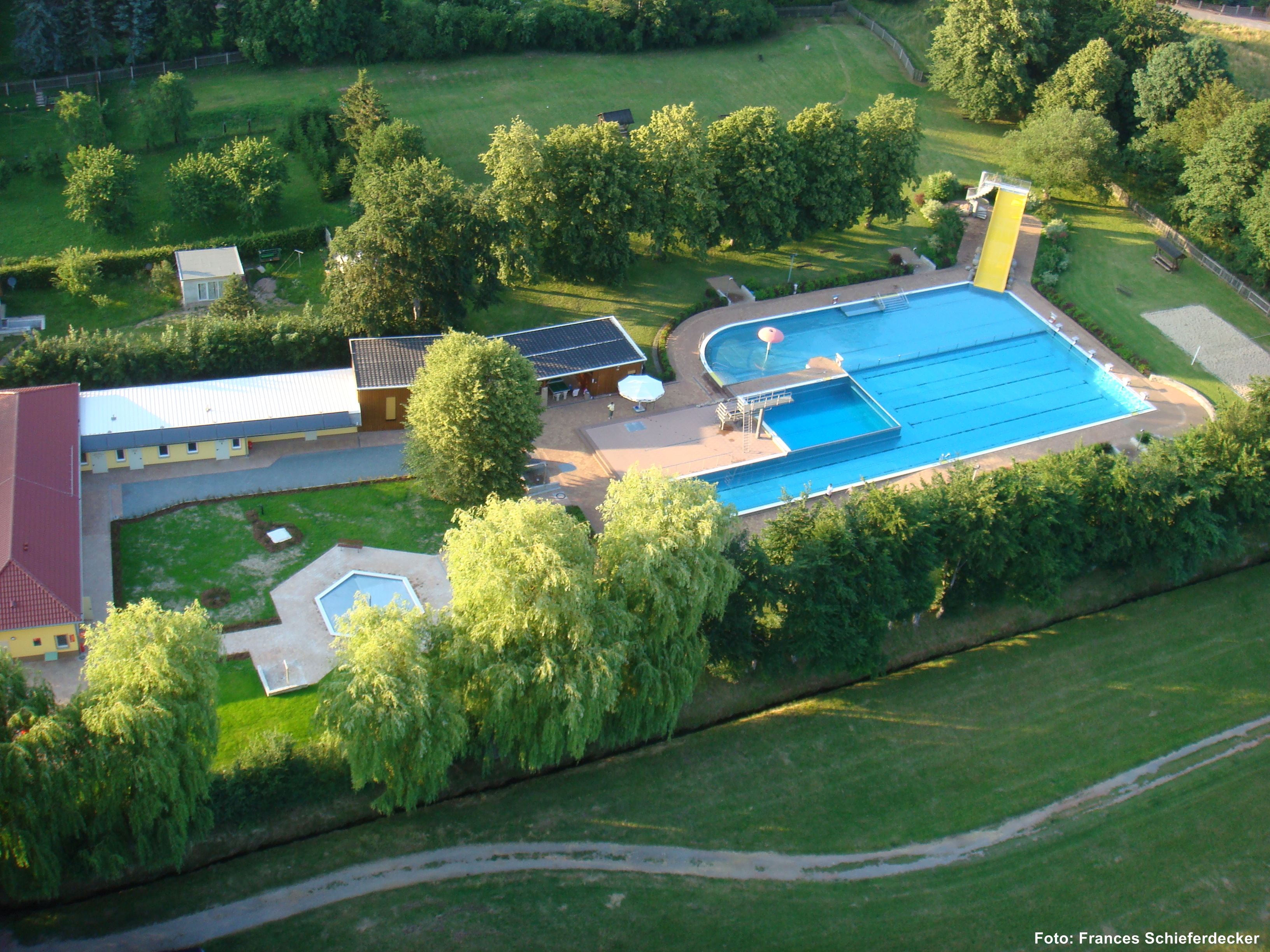 Das Bild zeigt eine Luftaufnahme, zu sehen sind Grünanlagen, Schwimmbecken und Gebäude.