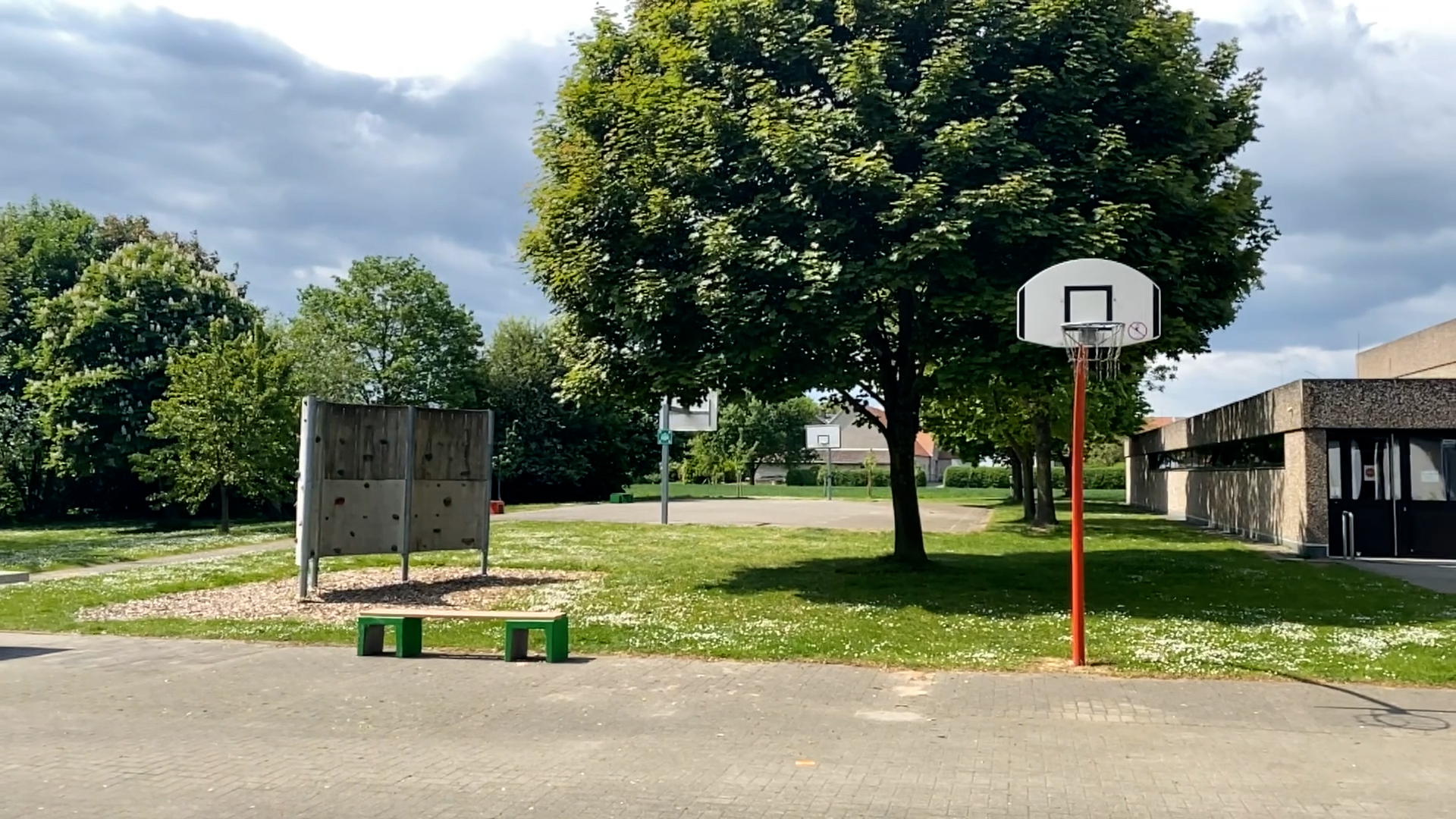 Das Bild zeigt einen Sportplatz mit Basketballkorb, Beachvolleyballfeld und Kletterwand. In der Mitte steht ein Baum, daneben eine Sporthalle.